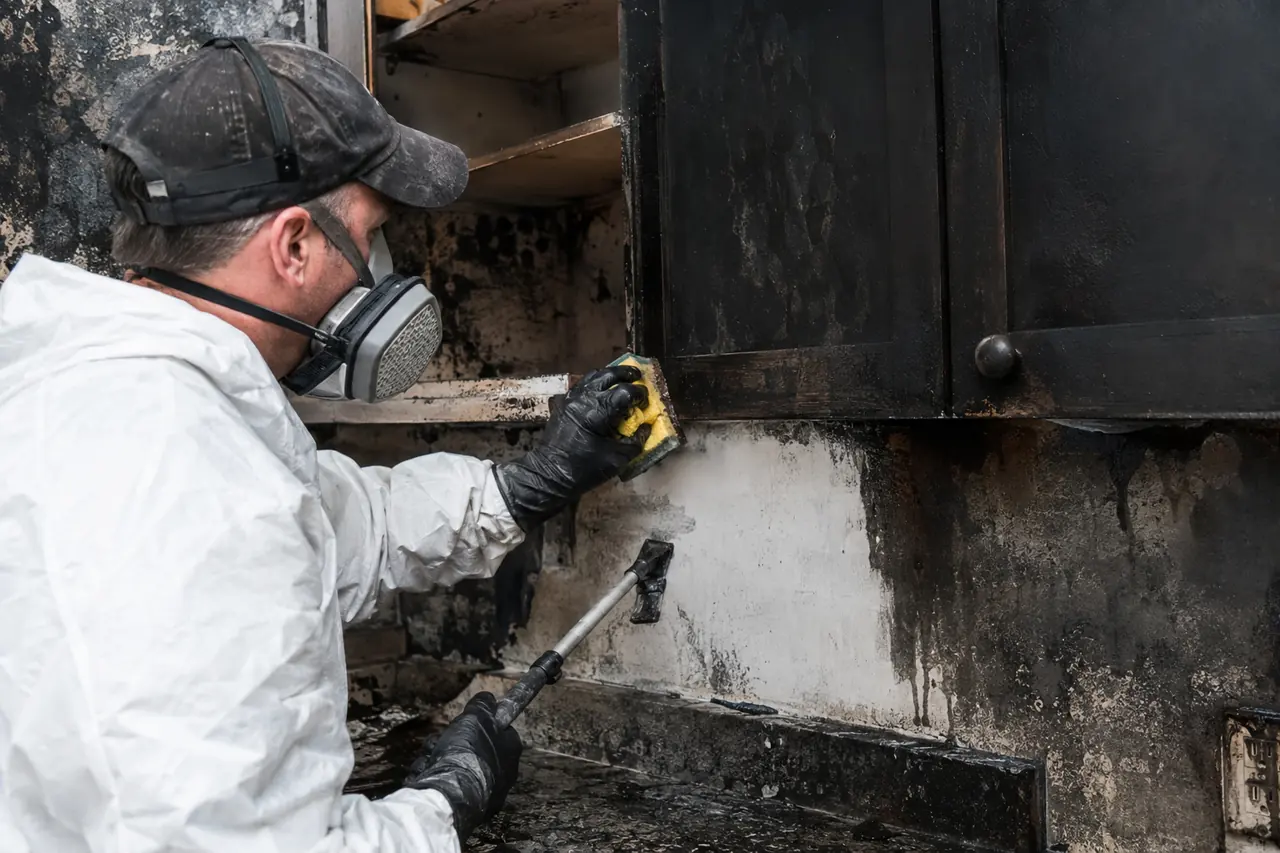 Worker in a respirator scrubbing soot from kitchen cabinets
